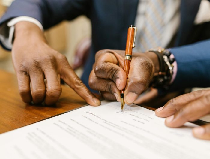 Close-up of business professionals signing a legal contract in an office setting.